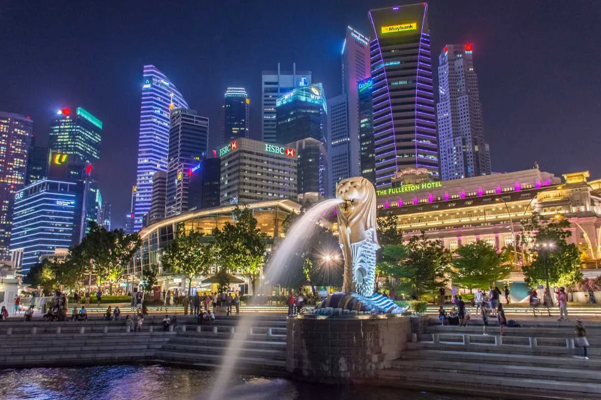  A wide view of Merlion Park SG near Fullerton Road, surrounded by palm trees and tourists.