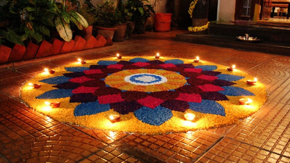A beautiful and intricate floor art made of colored rice and adorned with lit diyas, a traditional symbol of Diwali celebrations in India.