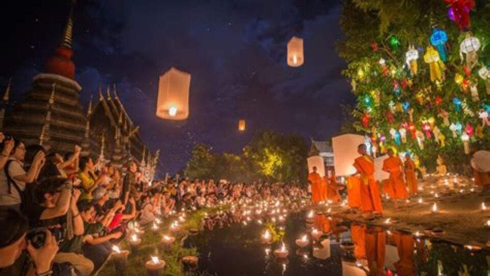 Monks lighting candles and releasing lanterns by the temple pond during Loy Krathong Festival in Chiang Mai, Thailand.
