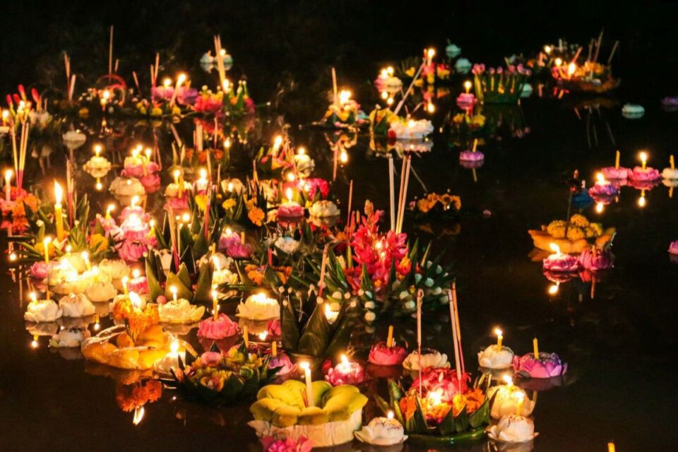 Floating krathongs with candles and flowers on a Thai river during Loy Krathong Festival.