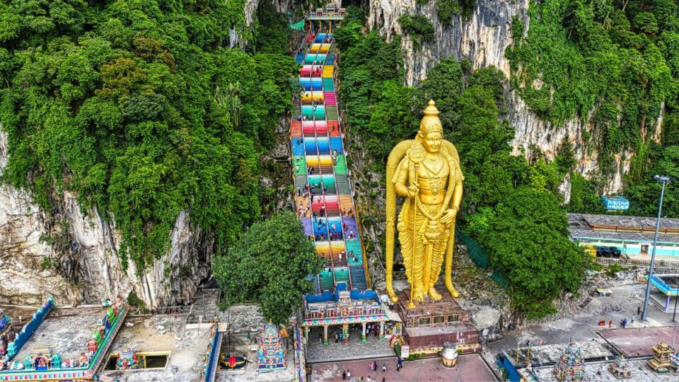 Giant gold Lord Murugan statue and colorful stairs during Thaipusam festival at Batu Caves.