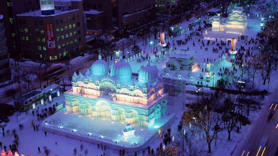 Aerial view of giant snow and ice sculptures illuminated at night in Odori Park during the Sapporo Snow Festival.